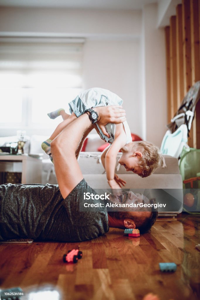 I Want To Fly Away! Father Having Fun With Baby Son In Living Room Family Stock Photo