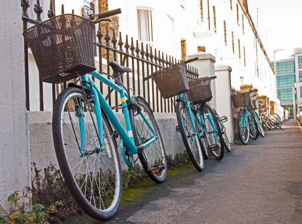 A row of matching rental bicycles with baskets are chained up to a fence outside a student house in Cambridge UK