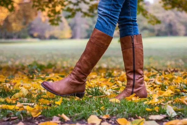 Photo of Woman wearing brown leather boot and walking in fallen leaves.