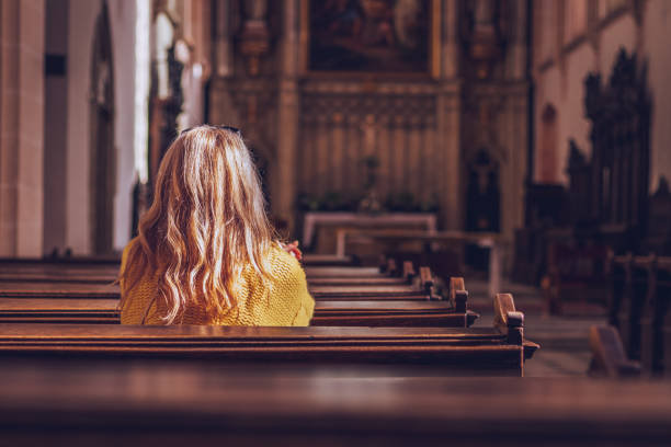 young woman praying and meditating in church. catholic cathedral with symbol of religion - church gothic style cathedral dark imagens e fotografias de stock