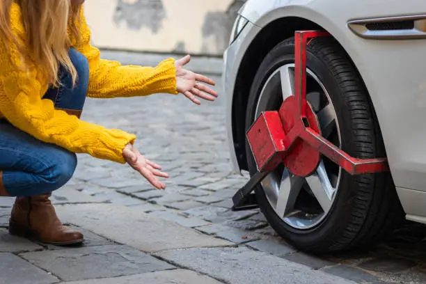 Photo of Upset woman looks at her parked car with wheel clamp.