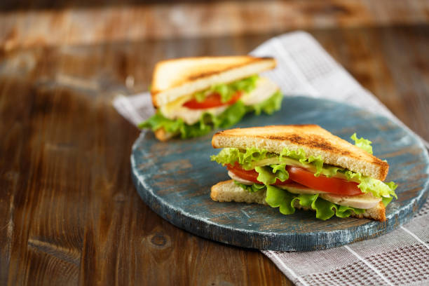 istock Appetizing sandwich with chicken, tomatoes, lettuce, cheese on a wooden plate on a dark background 1062564008