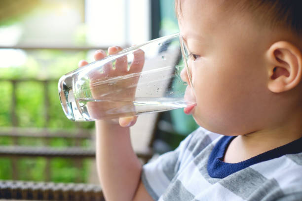 carino assetato piccolo asiatico bambino di 2 anni bambino bambino che tiene e beve vetro d'acqua da solo - 2 3 years immagine foto e immagini stock