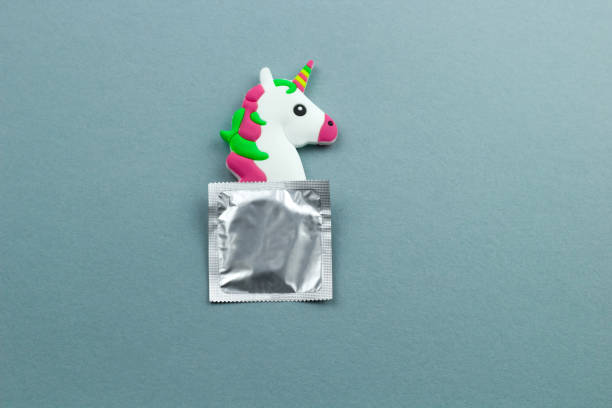 little unicorn toy head and condom  on a blue and green paper background - sex education condom contraceptive sex imagens e fotografias de stock
