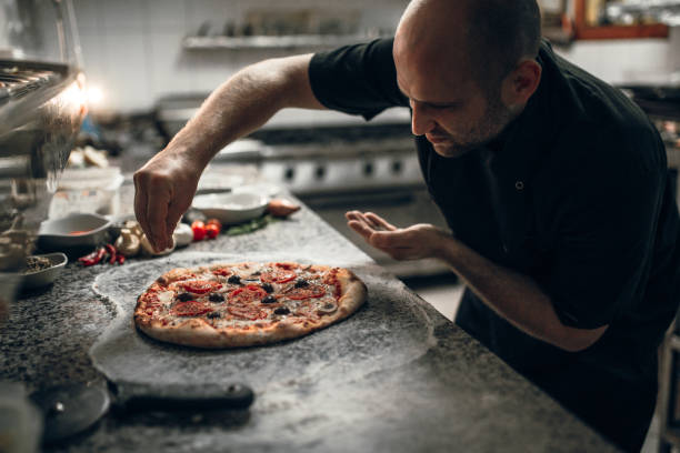 putting seasoning on pizza - pizzeria imagens e fotografias de stock