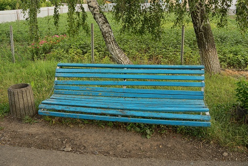 one old blue wooden bench and a gray urn in the green grass by the trees