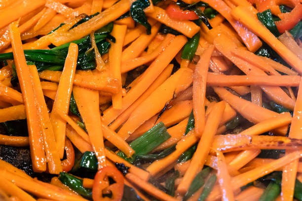 sliced carrots and scallion frying in pan close up