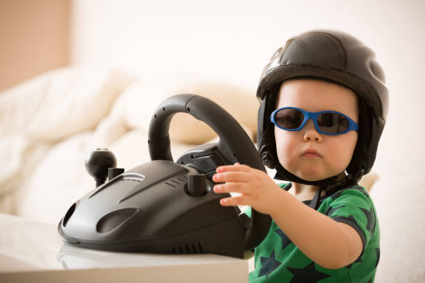 istock Cute little kid boy in a helmet playing with Computer steering wheel. Future driver. Getting ready for professional driving. Child driving a car. Funny toddler boy indoors. Boy and a car. 1062595966