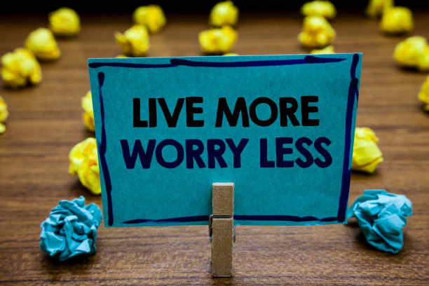 istock Handwriting text Live More Worry Less. Concept meaning Have a good attitude motivation be careless enjoy life Blurry wooden deck yellow and blue lob on ground paper clip grip page with text. 1062609770