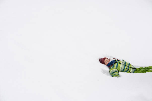 A smiling child wearing a dark jacket and neon scarf lies in deep powder snow, creating a playful winter moment. Perfect for family, kids, winter fun, outdoor activity, snow day themes.