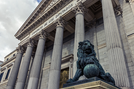 Main facade of the Spanish Parliament House with one bronze lion flanking the entrance (Madrid, Spain)