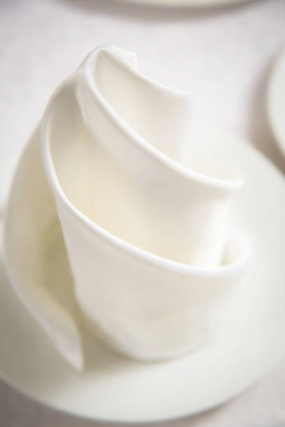 Beautiful white swirling napkin on a white plate.  White blurred background. Abstraction, serving a celebratory banquet