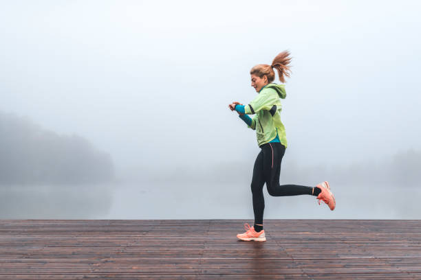 молодая спортсменка работает и проверяет пульс на смарт-часы на туманное утро - jogging running taking pulse women стоковые фото и изображения