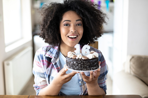 Smiling african woman holding birthday cake, looking at camera.