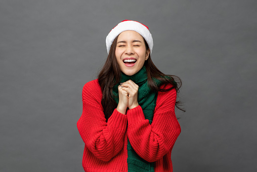 Young pretty Asian woman wearing red Christmas sweater and hat in surprised excited emotion