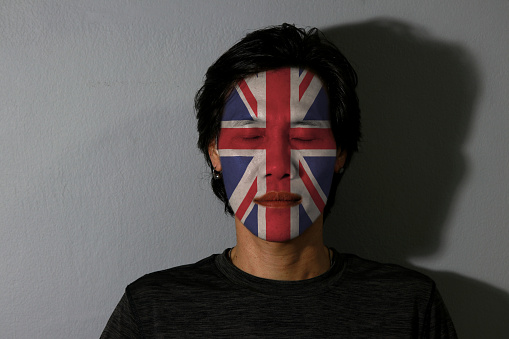 Portrait of a man with Union jack flag painted on his face and close eyes with black shadow on grey background. The concept of sport or nationalism.