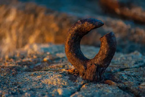 A broken metal eyebolt, covered in layers of flaking rust is embedded into rock, shot at sunset, it is bathed in soft golden light