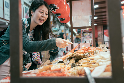 Japan travel lady pointing at the seafood on the mobile kitchen. girl tourist experience japanese culture. young traveler hungrily buying street food.