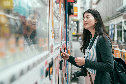 Japan vending machine. Young female tourist choosing a snack or drink at vending machine. lady putting coins into the vendor machine on the japanese street.