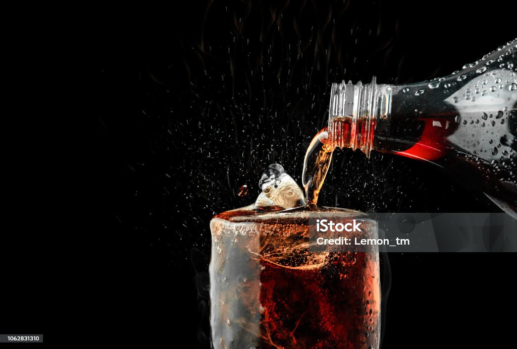 Pour soft drink in glass with ice splash on dark background. Cola Stock Photo