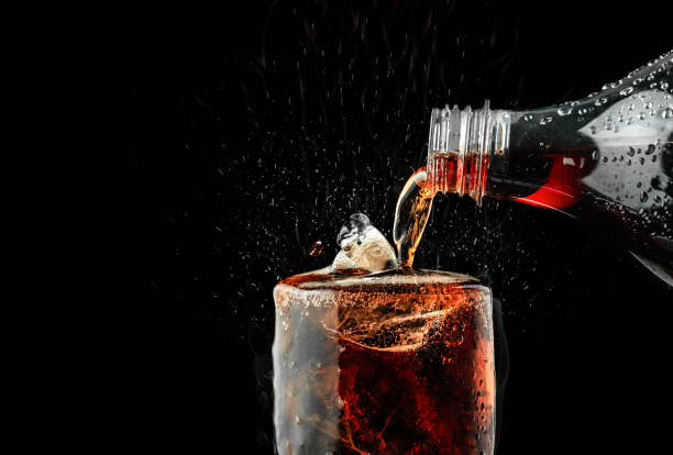 налейте безалкогольный напиток в стакан со льдом всплеск на темном фоне. - soda стоковые фото и изображения