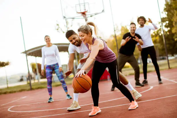 Photo of Group of multiracial young people   playing basketball outdoors