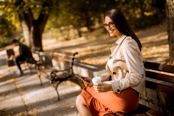istock Young woman drinks coffee and using digital tablet in the park 1062856486