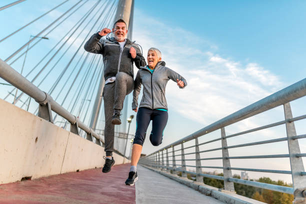 feliz pareja madura atlética saltando juntos - jumping women running vitality fotografías e imágenes de stock