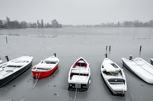 The small fishing boats are covered by the snow that falls on the frozen lake of Enghien-les-Bains