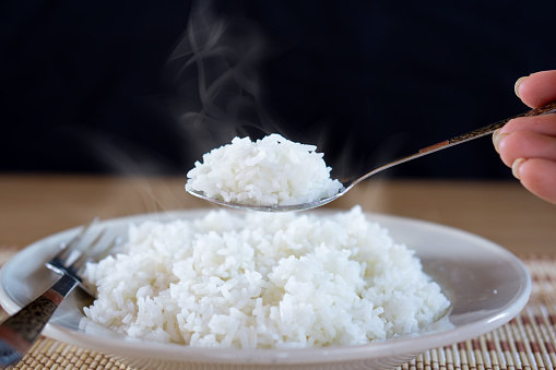 Asian woman hand eating cooked hot rice by spoon in a white plate