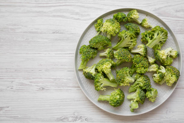 istock Freshly cut raw broccoli on gray plate on white wooden background, overhead view. Flat lay, from above, top view. Copy space. 1062885264