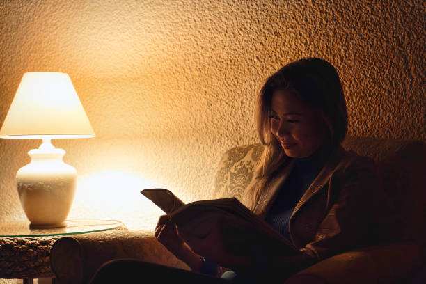 woman reading book in hotel lobby at night with low light - soft lighting imagens e fotografias de stock