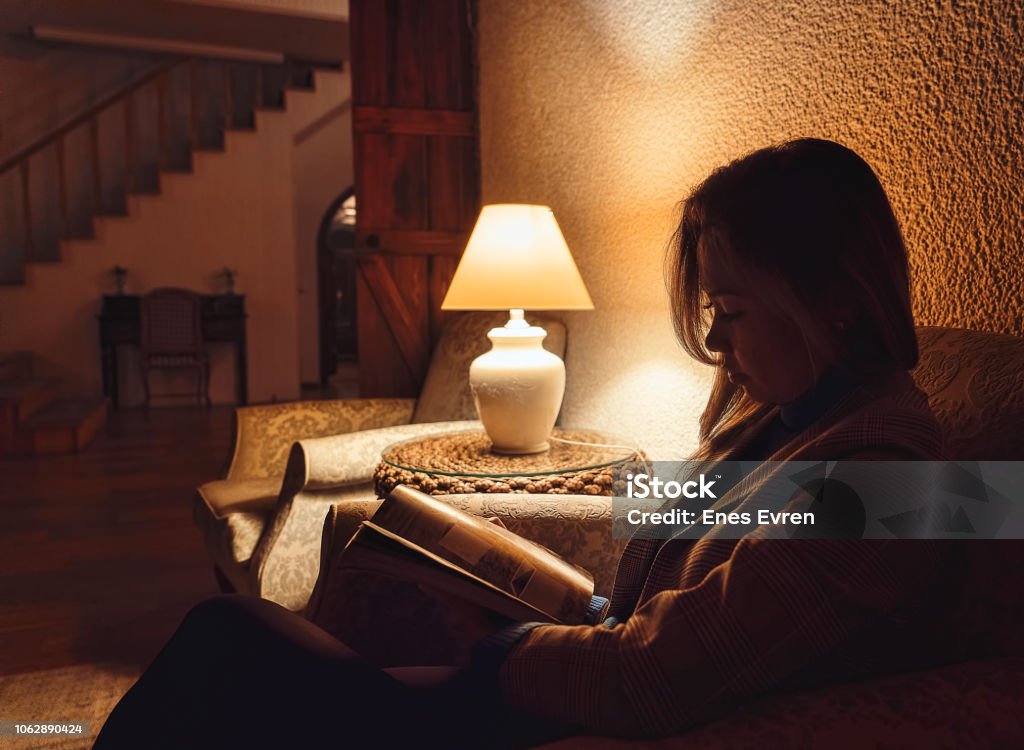 Woman reading book in hotel lobby at night with low light An Asian woman is reading a book in hotel lobby Low Lighting Stock Photo
