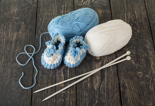 Knitted booties for baby, white and blue skein of wool yarn in dark boards