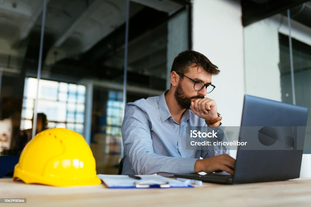 Engineer looking at laptop Photo of architect sketching at office Engineer Stock Photo