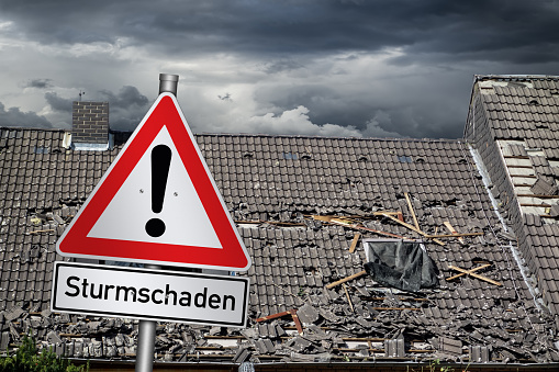 Achtung Sturmschaden german red warning sign in front of  storm damaged roof  ( english translation: attention storm damage )