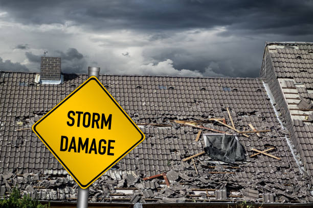 yellow damage warning sign in front of storm damaged roof of house stock photo