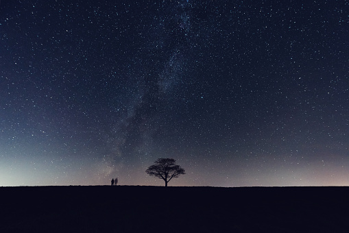A man walks through a field under the stars.  Long exposure.