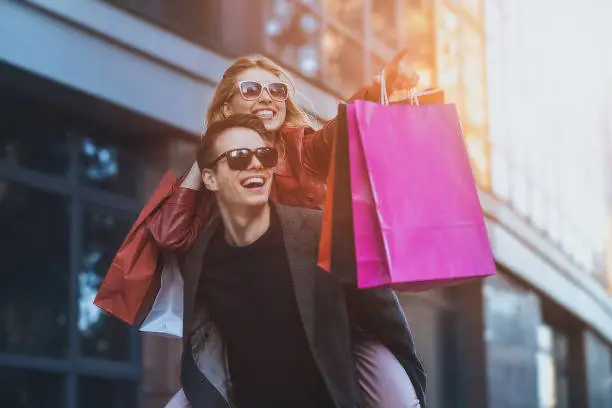 Photo of Couple in shopping together. Happy couple shopping together and having fun. Boyfriend carrying his girlfriend on the piggyback.