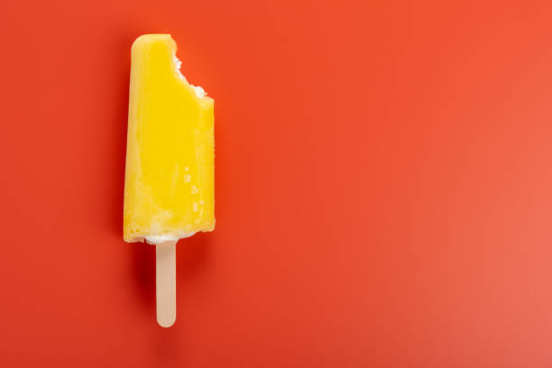istock yellow popsicle with a bite on an orange color background 1062932560