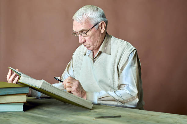 starszy mężczyzna w okularach bada poprzez powiększającą szklaną kolekcję znaczków pocztowych w albumie znaczków - neutral look audio zdjęcia i obrazy z banku zdjęć