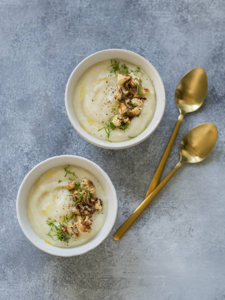 istock Cauliflower cream soup , decorated with fried cauliflower inflorescence in white bowls with golden spoons on a gray background. Top view 1062974980