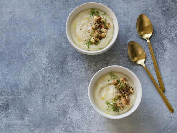 istock Cauliflower cream soup , decorated with fried cauliflower inflorescence in white bowls with golden spoons on a gray background. Top view 1062974986