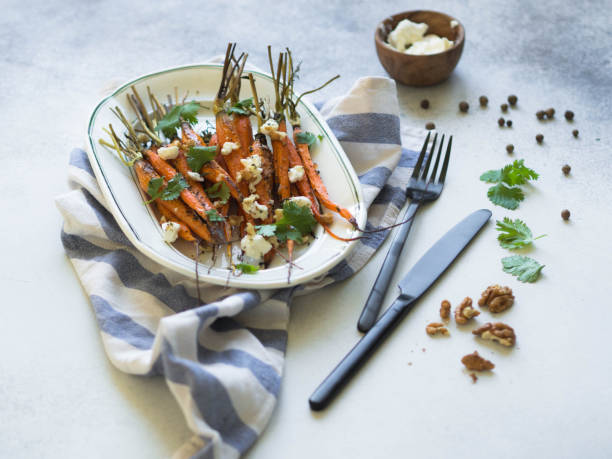 istock Baked young orange carrots with soft cheese, walnuts and cilantro on white oval plate. 1062975198