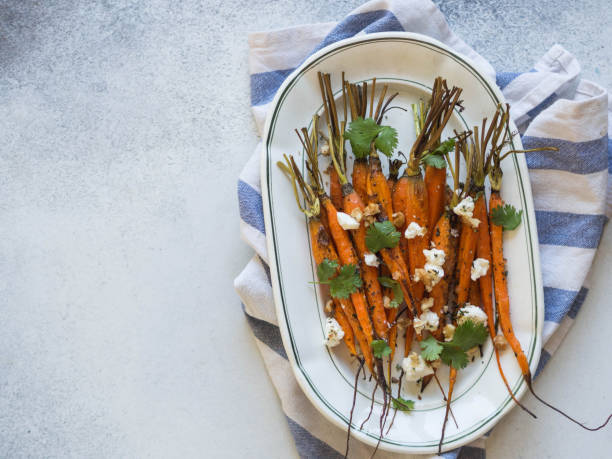 istock Baked young orange carrots with soft cheese, walnuts and cilantro on white oval plate. Top view. 1062975250