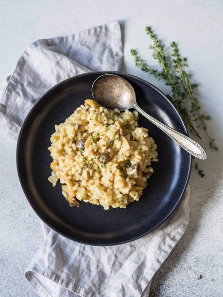 italienne risotto aux cèpes et thym frais dans une plaque noire sur un fond gris. maison végétarienne risotto aux champignons. vue de dessus - edible mushroom mushroom fungus porcini mushroom photos et images de collection