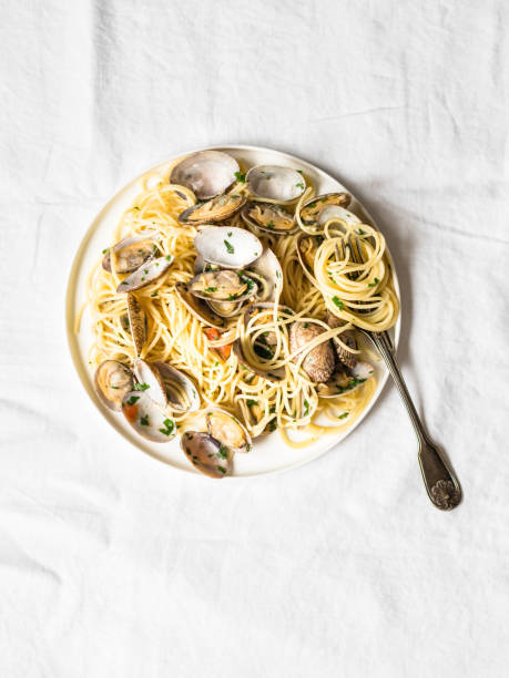 istock Spaghetti with clams, tomatoes, garlic and parsley on a white plate and rustic fork on a white background. Top view 1062975536