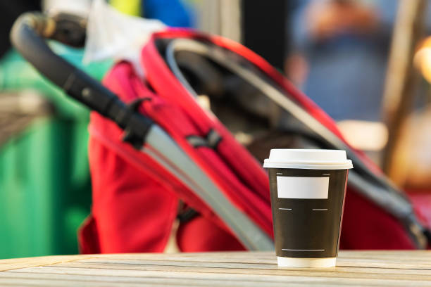 istock Paper coffee cup on a table with a stroller in the background. Parents relaxing concept. 1062982590