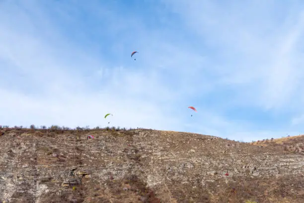 Photo of para-gliders on blue autumn sky flying near a cliff