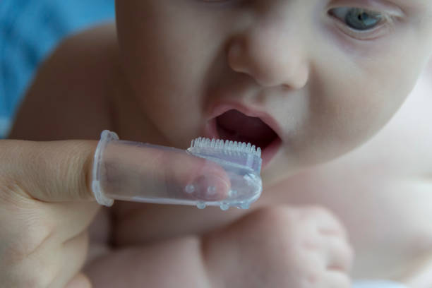 istock Mom brushes baby's teeth with a brush that fits on her finger 1063005938